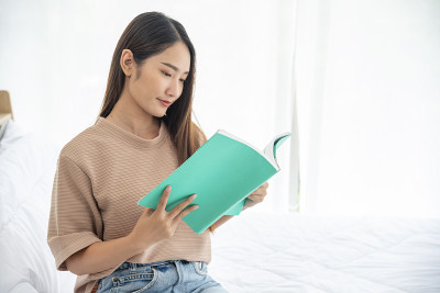 放松女人拿着书在大学图书馆的书架上阅读。少妇放松阅读，翻开书本，休闲心灵。聪明漂亮的女人聪明的人在知