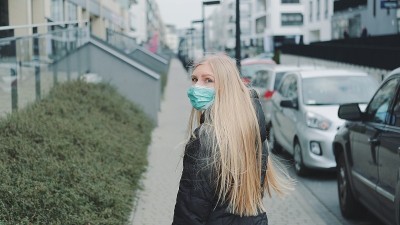 年轻的金发女人戴着医用面具在街上从某人身边逃跑