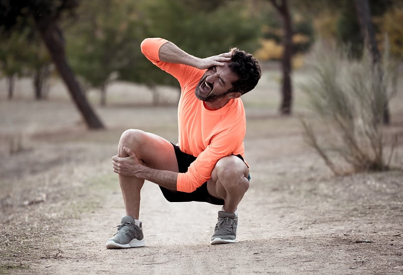 Young fit man holding knee with his hands in pain 