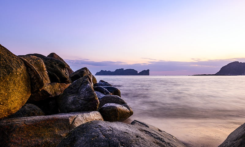 (长时间曝光)日落时美丽的热带海滩与岩石和平滑的水在前景和科皮皮李(玛雅湾)在远处的令人惊叹的景色。