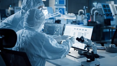 研究工厂洁净室:穿着工作服的工程师和科学家在计算机上交谈和工作，用显微镜检查主板微处理器，为医疗电子