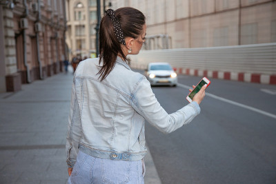 一个年轻女子在街上等出租车，手里拿着电话