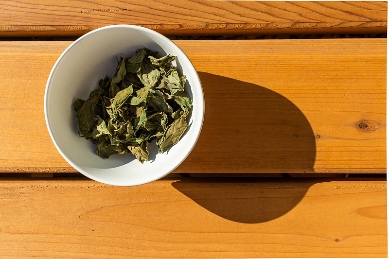 Dehydrated basil in a bowl on wood surface