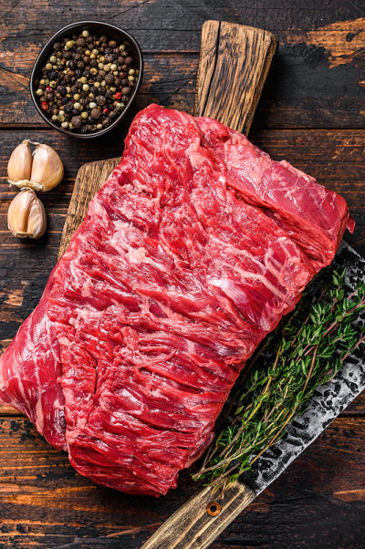 大块生牛胸肉，配香草和切肉刀。深色木制背景。俯视图