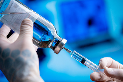 医生手持白手套，手持疫苗和注射器。蓝色实验室SARS冠状病毒的药物
