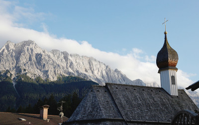 传统的瓦屋顶和一个小洋葱圆顶塔。以山脉为背景，Waxenstein和Zugspitze山峰的房子。