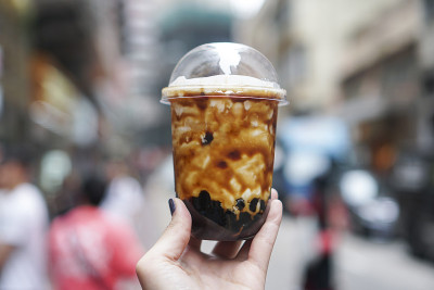 女人拿着一个塑料杯新鲜牛奶和红糖波巴/泡沫饮料。