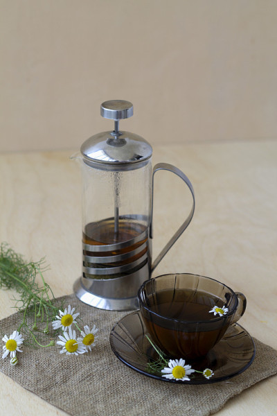 深色玻璃杯里放着一杯凉茶和甘菊茶，放在一张有复印空间的轻木桌上。茶杯和茶壶，花束鲜花和绿色的叶子在黄