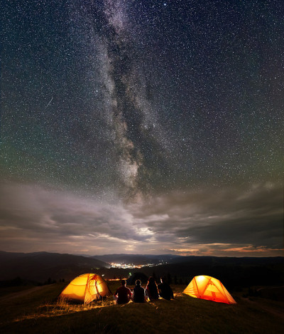 后视图三名游客坐在帐篷营地享受火苗在夜空下的星空