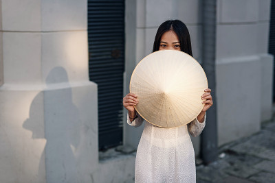 可爱快乐的亚洲女孩穿着敖代的衣服关闭她的一半脸与越南锥形帽子。