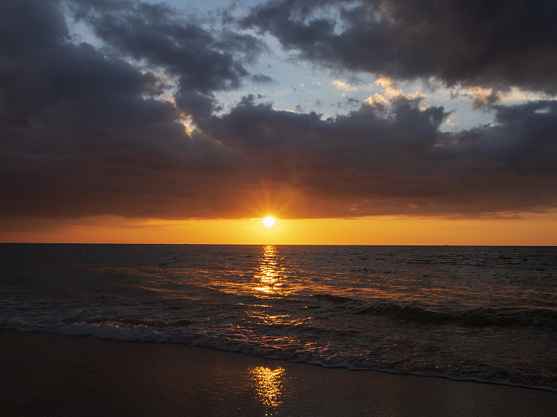 美丽的日落在平静的海上与云天空的背景。热带海滩上的日落。夏天自然的概念。海上的日落高峰，黄色的光线反