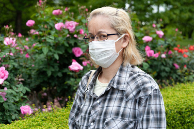 中年混血儿金发女人戴眼镜戴白色外科口罩。预防COVID-19和其他传染病。在户外。可疑的看