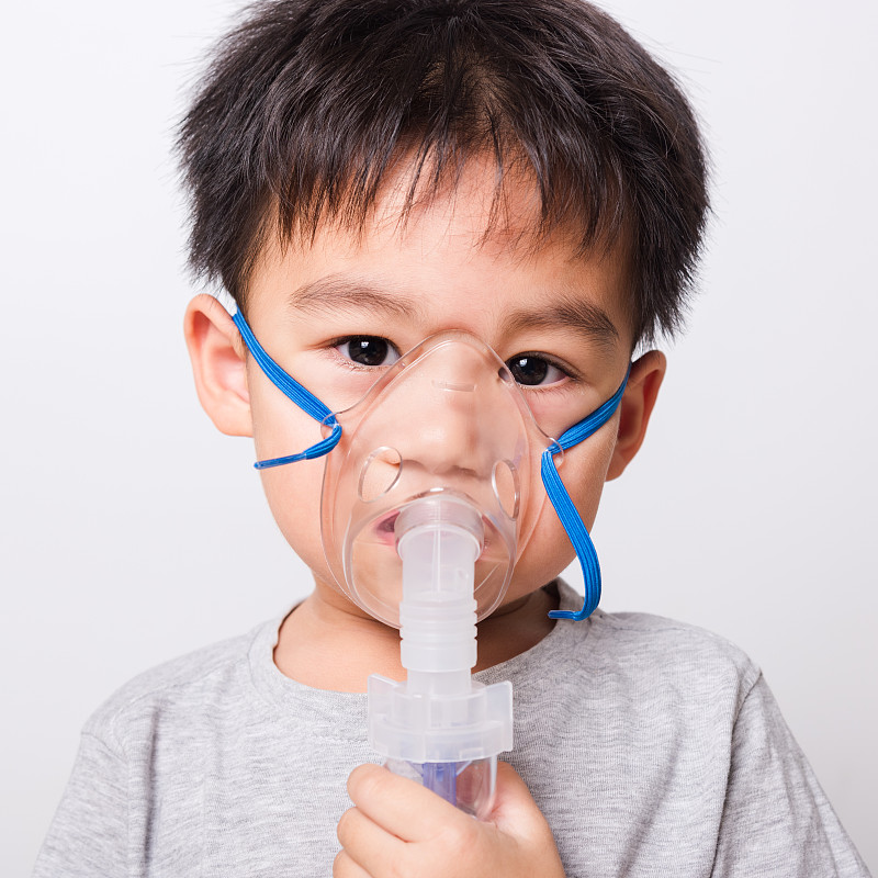 特写亚洲脸，生病的小孩他用蒸汽吸入器雾化面罩吸入自己的白色背景