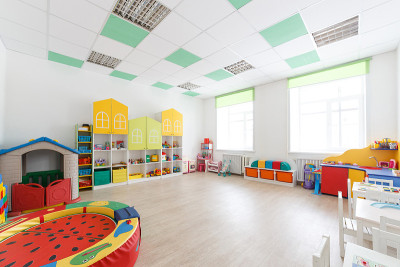 幼儿园里宽敞的白色游戏室里有玩具，两扇大窗户和上课用的桌子