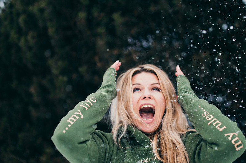 迷人的斯堪的那维亚金发女郎穿着绿色的帽衫正在玩雪