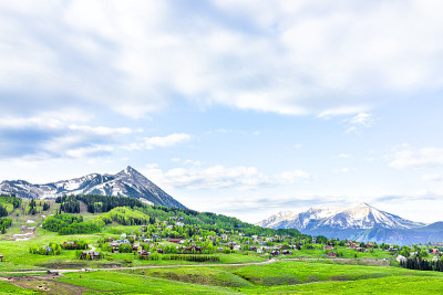 山顶山顶全景雪山与多云的天空在郁郁葱葱的绿草夏天与房屋建筑在小城镇的村庄