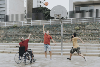 一个坐轮椅的人和他的朋友在城市公园里打篮球。