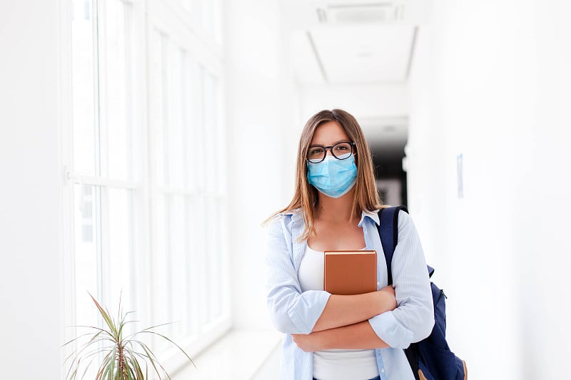 学生戴着防护口罩在空旷的大学室内。高中要参加考试的年轻女子。