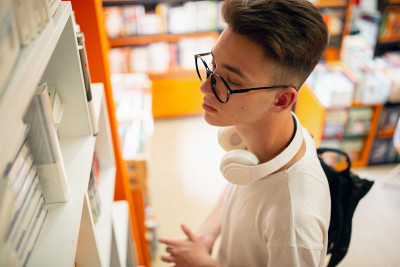 拿着书的男大学生站在图书馆的书架旁。