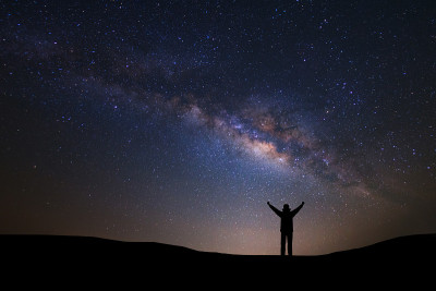 宇宙中有银河和太空尘埃的景观，夜空中有星星和一个站在高山上举起手臂的运动员的剪影。