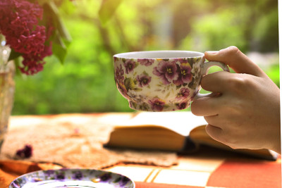 手持瓶中有丁香花束的茶杯和书