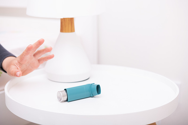 一个小男孩伸出手去寻求帮助，桌上放着一个哮喘吸入器