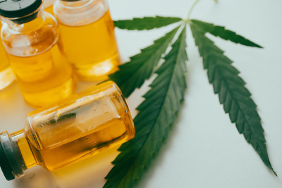 小瓶中的大麻油，白色背景上有一片绿叶。替代医学概念。