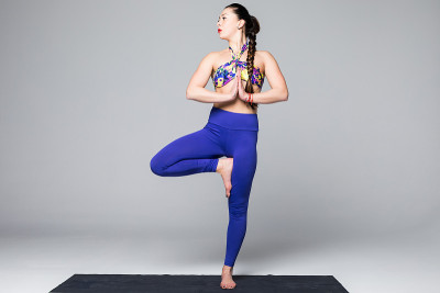 Vrikshasana。美丽的瑜伽女人练习瑜伽姿势在灰色的背景。