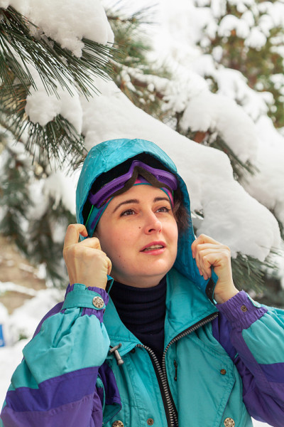 穿着滑雪服的女孩站在高大的松树下