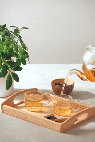 一只手从放在木托盘上的玻璃茶壶里倒茶