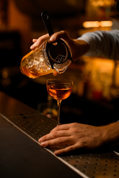 调酒师的手轻轻地拿着一个有滤网的搅拌杯，将液体倒入酒杯