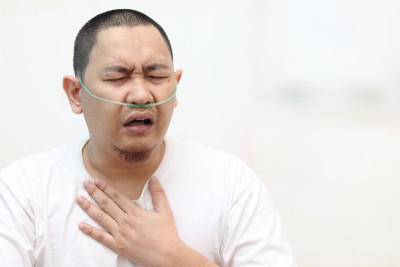 患有哮喘的亚洲男子，手碰到胸部时呼吸困难。住院Covid-19患者出现呼吸障碍，鼻内插氧气管