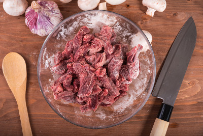 烹饪蘑菇炖牛肉，俄式牛肉-生牛肉块，面粉去骨，在一个玻璃碗，俯视图。
