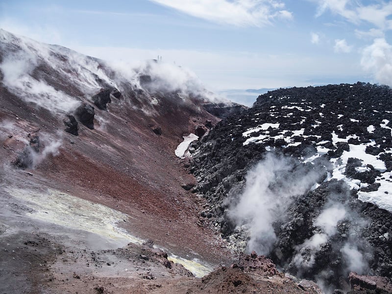 男人们在阿瓦钦斯基层状火山(也被称为阿瓦查火山)的破火山口远足的剪影。背包客们在炽热的间歇泉蒸汽后面