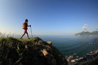 女徒步旅行者徒步在日出的海边山径