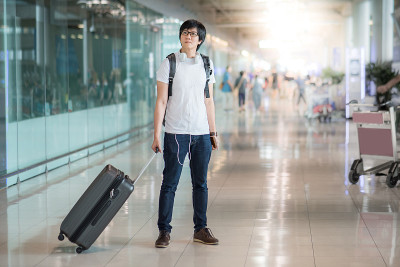 一个年轻的亚洲男子带着他的行李箱在机场候机厅等待