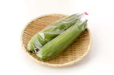 新鲜的绿色丝瓜或丝瓜放在塑料袋里，竹筛放在白色的背景上