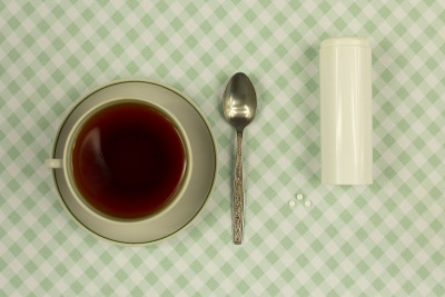 三片小白糖代替药片，旁边放一杯茶和一个药片储存罐。一粒代替一茶匙的糖