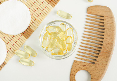小的白色碗，装有化妆油(血清，鳕鱼油)胶囊和木质发刷。天然spa、护发美容配方。俯视图，复制空间。