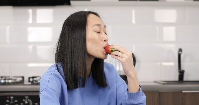 年轻的亚洲女子在室内吃新鲜草莓。