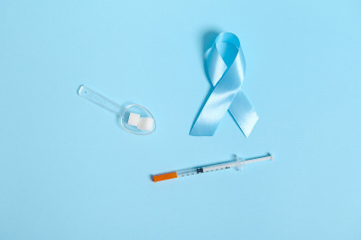 平整的胰岛素注射器，测量勺上的方糖和蓝丝带，象征着11月14日世界糖尿病意识日。蓝色背景的医学概念广