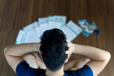 俯视图紧张的年轻亚洲男子双手抱着他的头，想着找钱来支付信用卡债务和所有的账单。