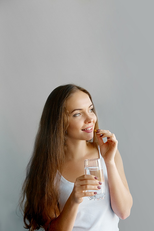 健康饮食,生活方式。快乐微笑的女人服用鱼肝油欧米伽-3丸的近距离观察，在早上拿着一杯淡水。维生素D,