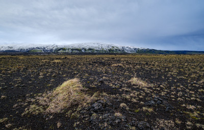 冰岛，秋天冰雪覆盖下多彩的曼那洛加山。前景是火山沙的熔岩场。