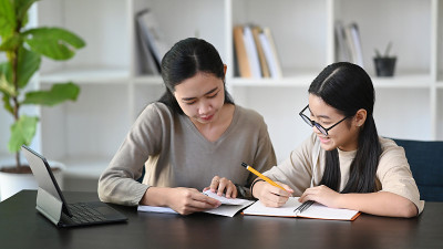 细心的亚洲母亲帮助女儿做家庭作业在家里。
