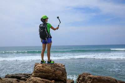 一名女子在海边徒步旅行，用动作相机自拍