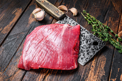 切肉刀上的生牛腩肉。深色木制背景。俯视图