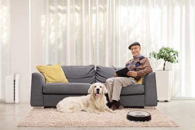 家里有一位老人和一只猎犬，还有一个机器人吸尘器在清洁地毯