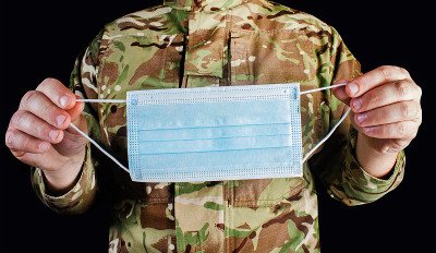 身着迷彩服的士兵在黑色背景上拿着医用防护面罩。