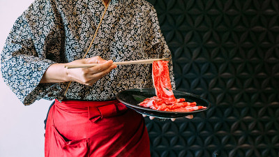身着和服的妇女用筷子夹着鲜嫩的和牛A5牛肉片在素喜烧火锅中煮。
